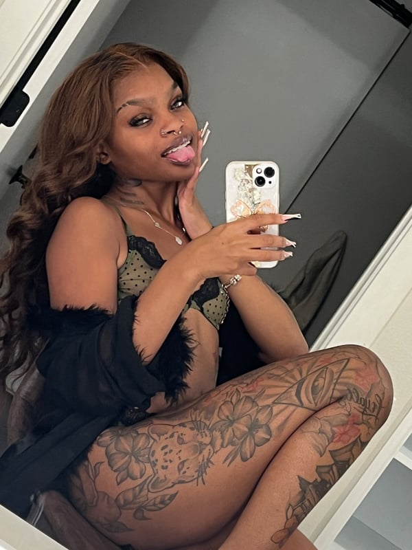 A woman taking a mirror selfie in a bedroom, wearing lace top and fur-trimmed robe while holding her phone.