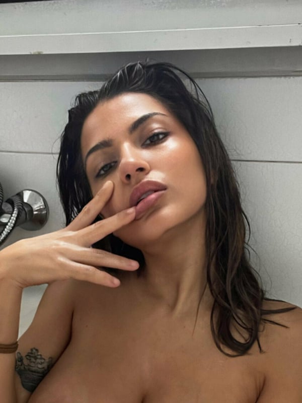 A woman with wet hair making a gesture in a bathroom near a bathtub.