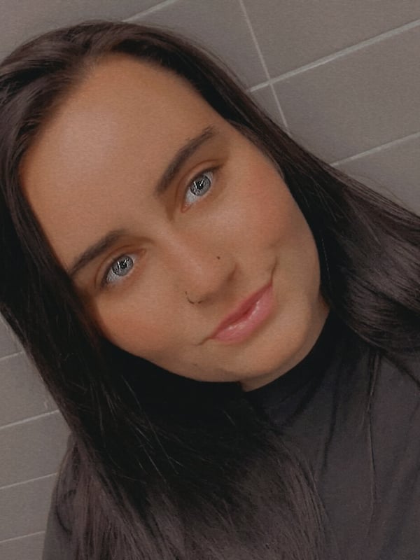 A young woman with long dark hair smiling at the camera against a plain gray background.