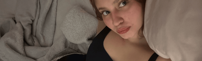 A young woman reclining on a bed in a black top, looking toward the camera.