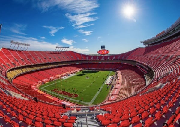 Aerial view of a large red stadium with a green football field under a clear blue sky.