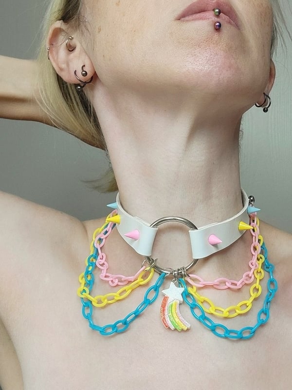 Close-up portrait of a young woman with blonde hair, lip piercing, and colorful spiked collar necklace.