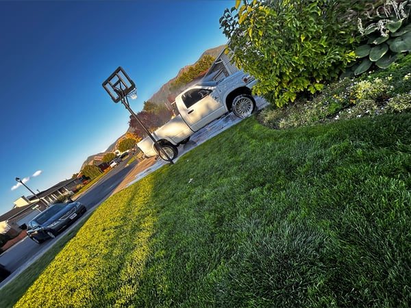 Scenic outdoor view of a residential driveway with a white pickup truck, basketball hoop, and surrounding greenery under a clear blue sky.