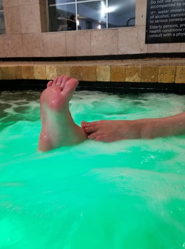 Close-up view of a person's foot extended over bubbling green water in a hot tub at a spa facility.