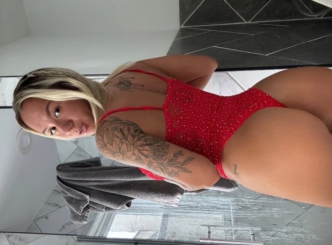 A woman posing in a sparkling red swimsuit in front of a bathroom mirror with tiled walls.