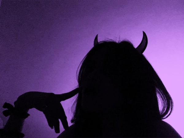 Silhouette of a person with devil horns posing playfully against a vibrant purple background.