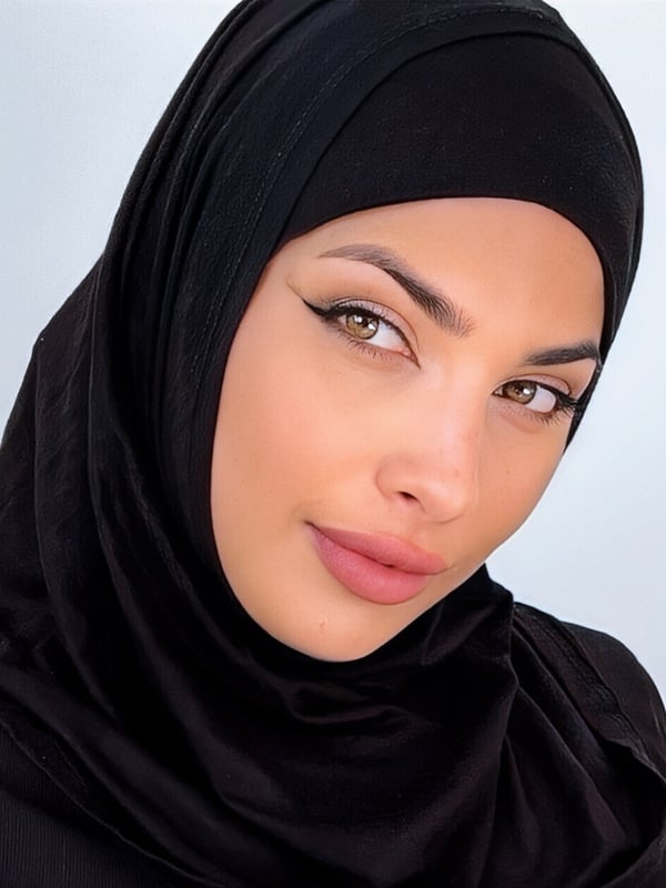 Close-up portrait of a woman wearing a black headscarf, with subtle makeup and a calm expression.