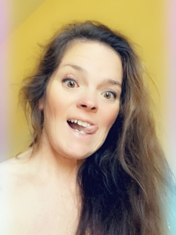 Close-up portrait of a smiling woman with long brown hair against a yellow background.