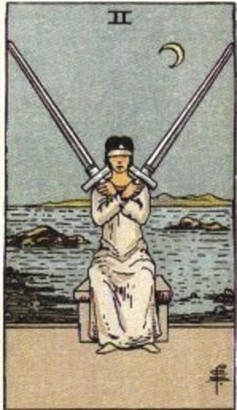 Tarot card illustration of a blindfolded figure seated between two swords against a scenic watery background with a crescent moon.