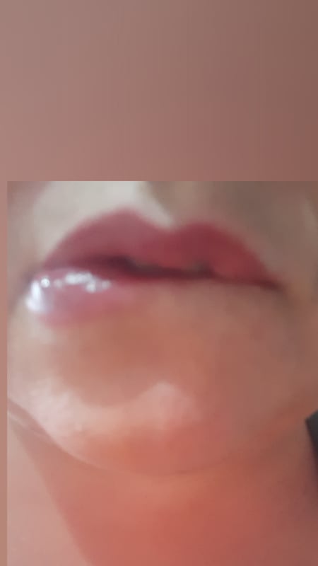 Close-up of a person's glossy red lips in a soft-focus portrait.