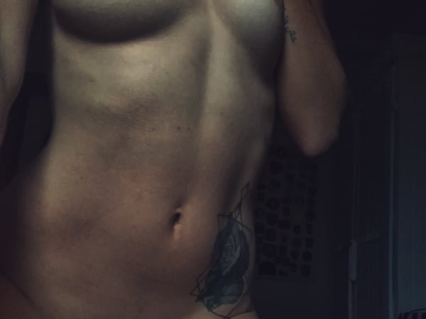 A person posing with visible tattoos in a dimly lit indoor setting.