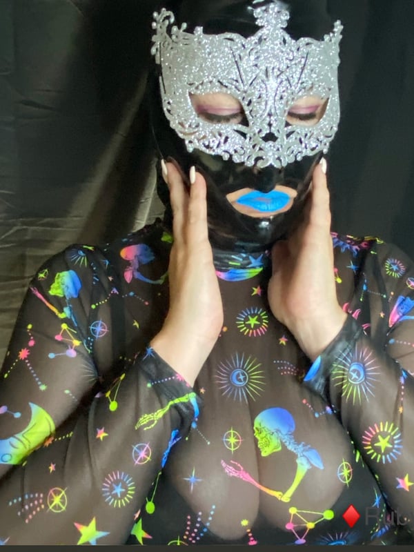 Close-up of a person wearing an elaborate silver and black mask with blue lipstick, framed by a colorful patterned top.