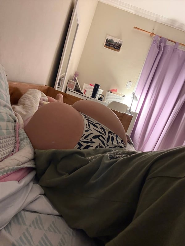 A young woman lying on a bed in a bedroom, wearing underwear and a top, posing relaxed against pillows.