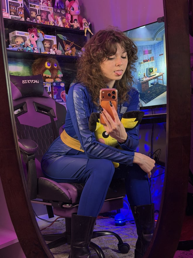 A woman wearing a cozy animal-themed costume and face covering, seated in a colorful room with plush toys.