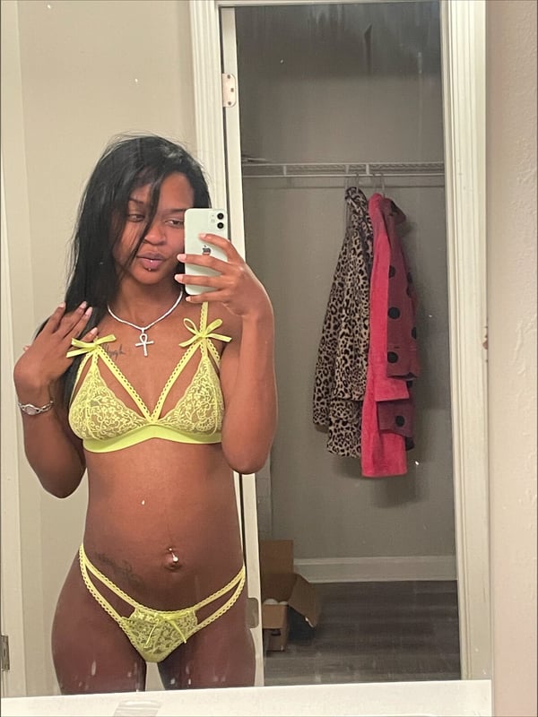 A woman taking a mirror selfie in a bright yellow lace outfit in front of a closet.