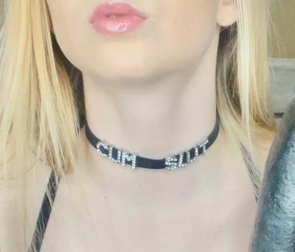 Close-up portrait of a woman with long blonde hair wearing a black choker necklace against a neutral background.