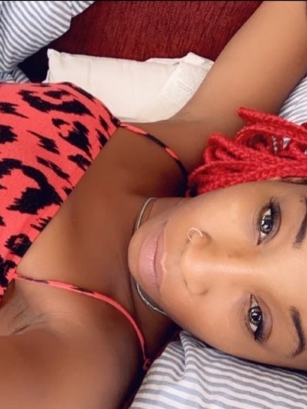 Young woman with red braided hair lying on a bed, wearing a leopard-print top, posing with a relaxed expression.