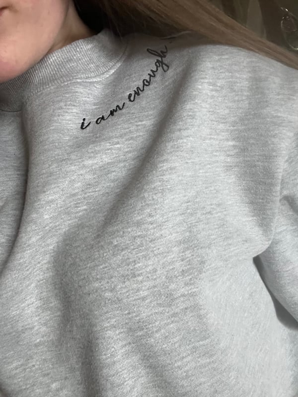 Close-up of a person wearing a gray sweatshirt with embroidered text, smiling softly.