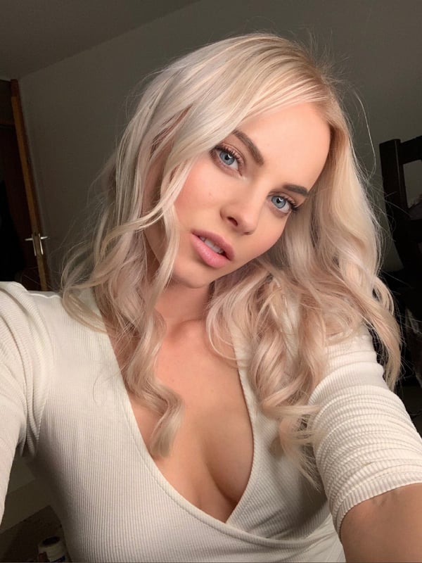 A close-up selfie of a woman with long blonde hair wearing a white top.