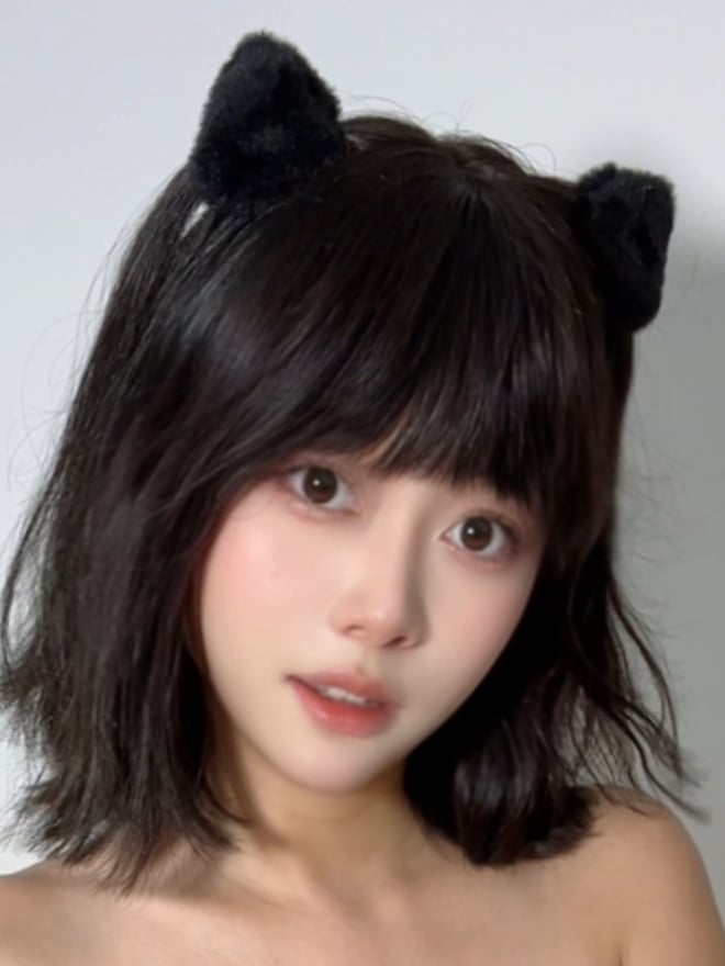 A young woman with shoulder-length dark hair and black cat ear headbands smiling softly against a plain white background.
