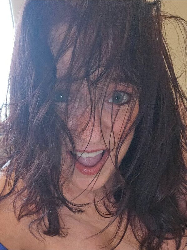 Close-up portrait of a smiling woman with wavy red hair and green eyes, wearing a blue top.