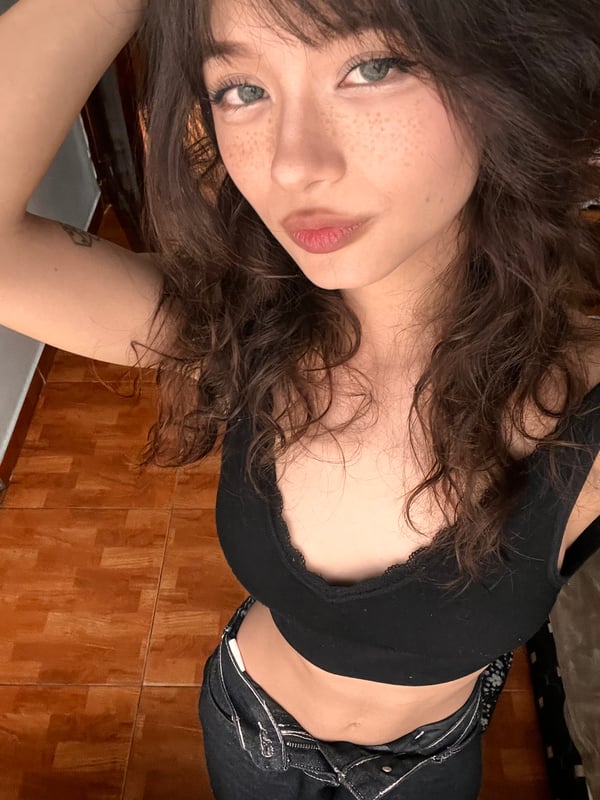 A person wearing a cat-ear headband and glasses, posing playfully while wearing a black outfit.