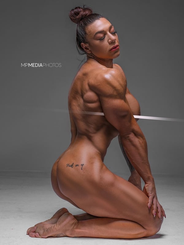 A muscular woman in a rear pose highlighting her defined back and strong build against a dark background.