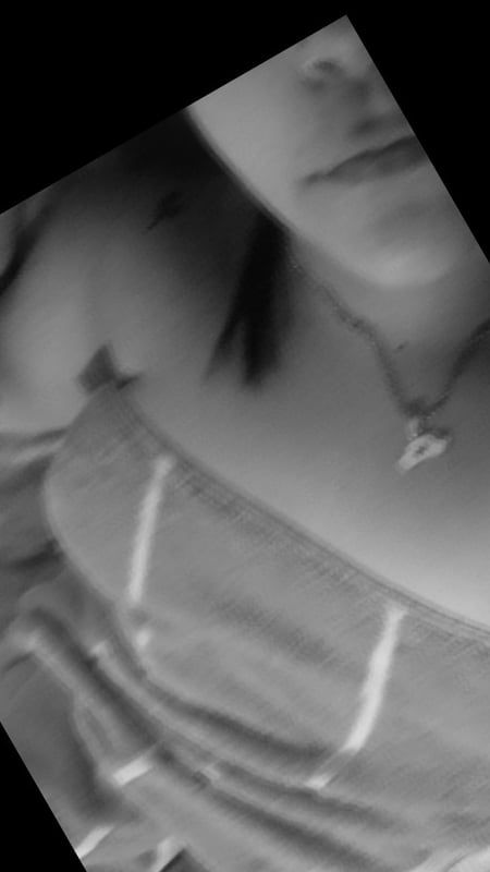 Close-up portrait of a woman with dark hair wearing a necklace, posed sideways in soft lighting.