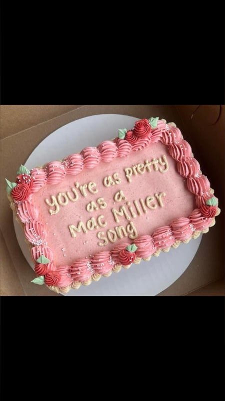 A pink cake with strawberry decorations and the text 'You're as pretty as Mac Miller song' written in white frosting.