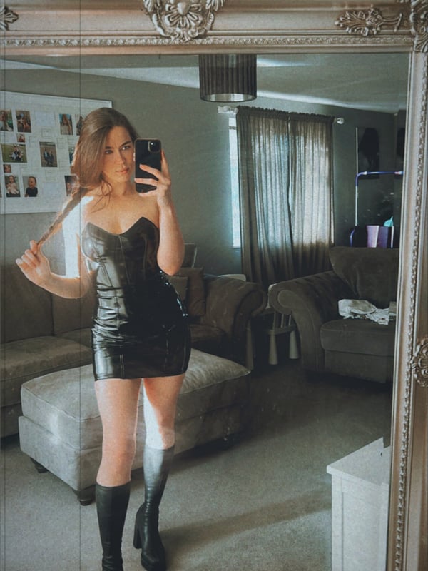 A person standing in a living room, posing confidently in front of a mirror while holding a phone.