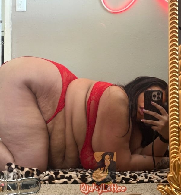 A woman in red lingerie posing on the floor in front of a mirror with neon lights and a decorative frame.
