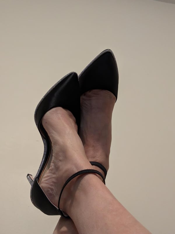 Close-up of a woman's legs and feet wearing black high-heeled shoes with ankle straps.