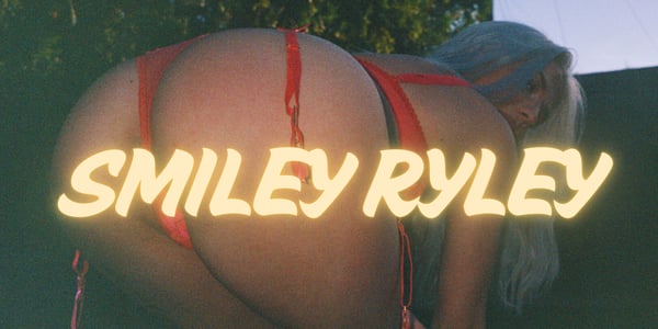 A woman posing in a red swimsuit against an outdoor background with her username overlaid in bright text.