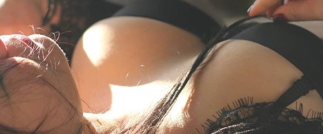 A woman lying on her side in black lace lingerie, posing seductively with soft lighting.
