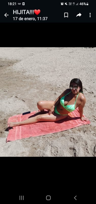 Woman in green bikini lounging on a beach towel on the sand, wearing sunglasses.