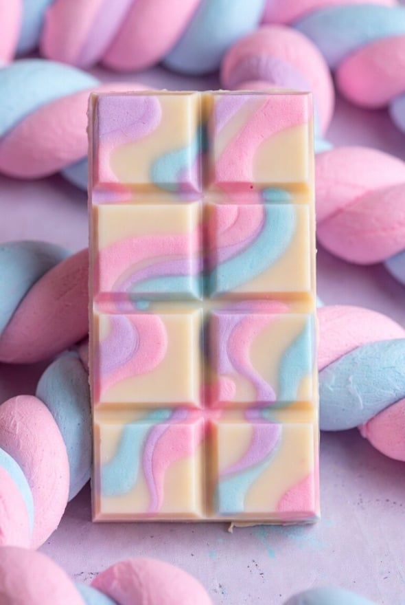 Close-up of colorful marshmallows and swirled white chocolate arranged on a purple background.