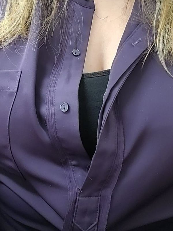 Close-up of a woman with long blonde hair wearing a partially unbuttoned purple blouse, smiling confidently.
