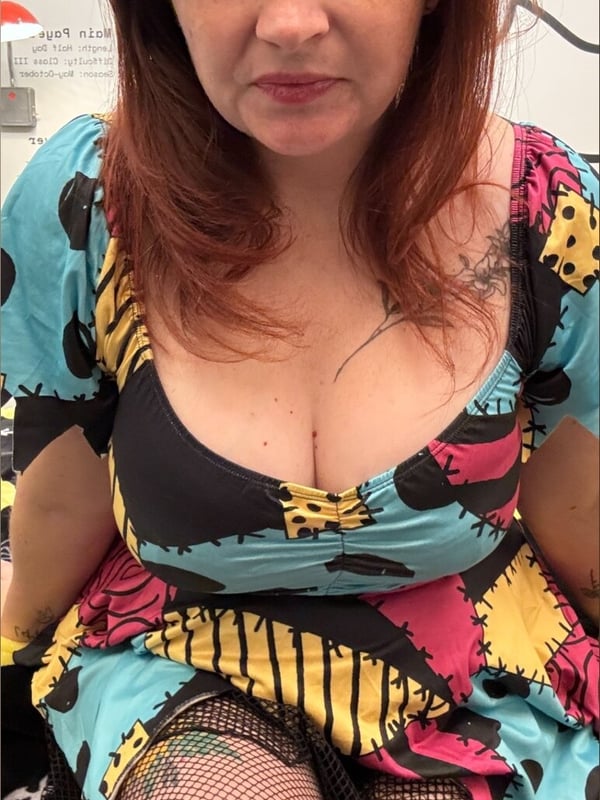 A woman with red hair wearing a colorful Sally costume from The Nightmare Before Christmas, posing with a serious expression.