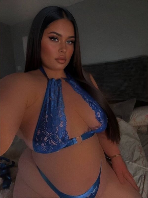 A woman taking a selfie in a blue lace top while sitting on a bed.