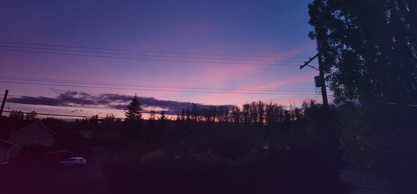 Scenic sunset view over a rural landscape with trees, power lines, and houses in the background.