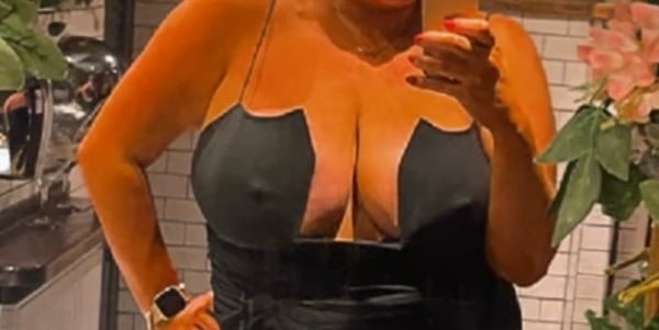 A woman posing in a black top with plants and kitchen elements in the background.