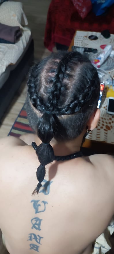 A man with braided hair and tattoos on his back, posing shirtless in a home setting with casual indoor background.