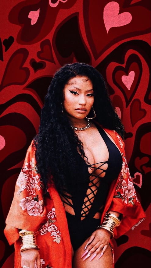 A woman with long wavy hair posing confidently in a black outfit with an orange floral robe against a vibrant red heart-patterned background.