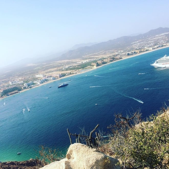 Scenic aerial view of a coastal city with a large cruise ship in the bay, surrounded by mountains and ocean waters.