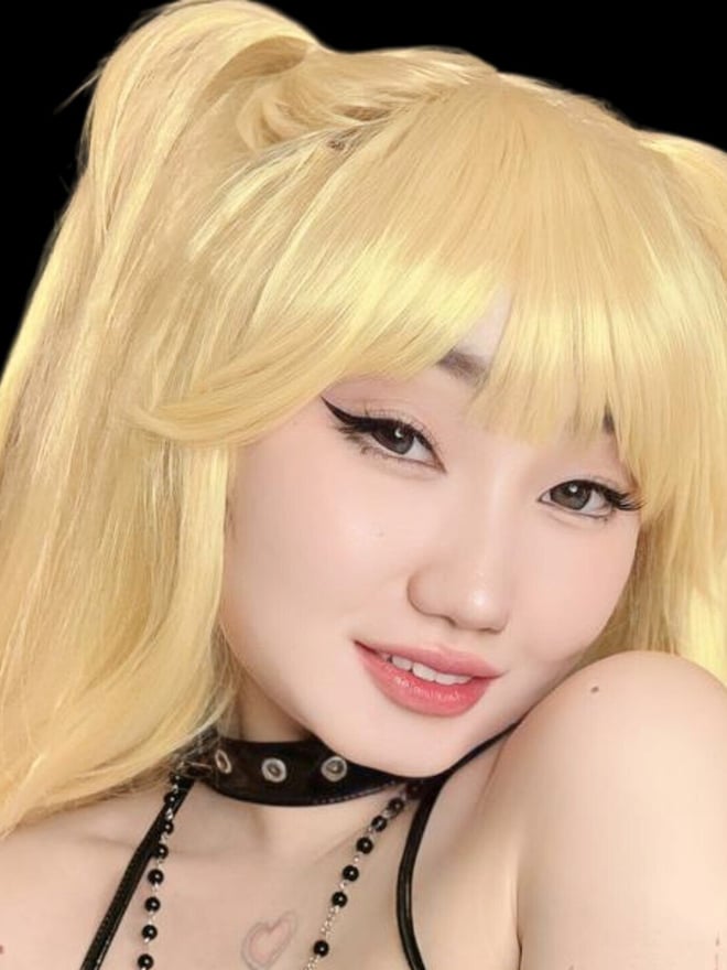 A blonde woman with cat-ear-inspired styling poses in a black choker and layered accessories against a dark background.