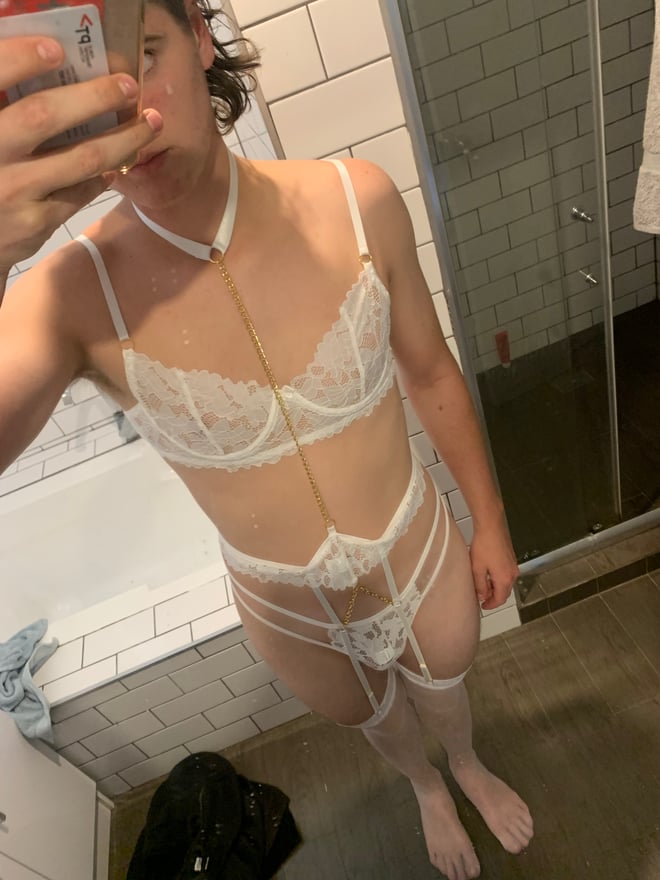 Person taking a mirror selfie in a bathroom, dressed in white lace lingerie and garter straps.