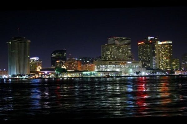 Nighttime city skyline with illuminated skyscrapers reflected on a calm body of water.