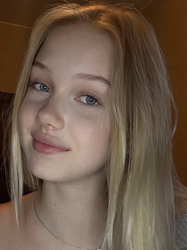 Close-up portrait of a young woman with long blonde hair and blue eyes wearing a delicate necklace.