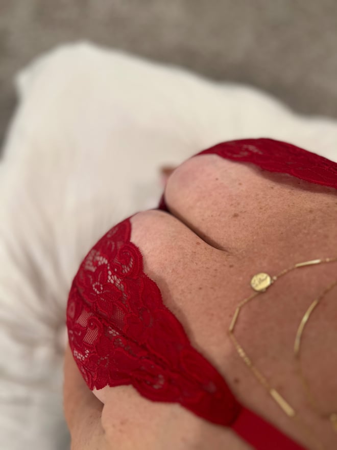 Close-up of a person in red lace top lying on a white surface, wearing a gold necklace.