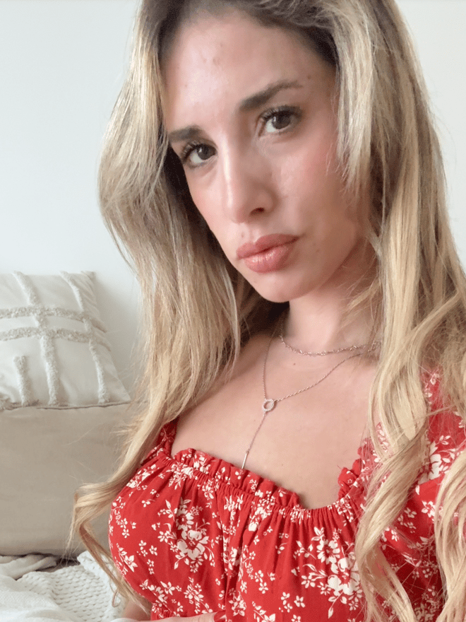 A blonde woman taking a close-up portrait in a red floral top indoors.